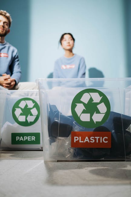 A flat lay image on a wooden surface showing a white sheet of paper with a large green recycling symbol printed on it, surrounded by various household waste items. In the top left corner, there is a w